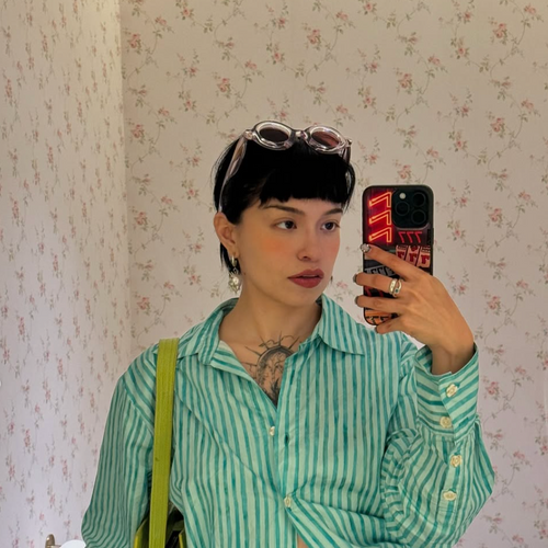 Person taking a mirror selfie wearing a green striped shirt with floral wallpaper background