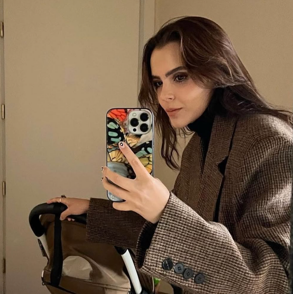 Woman taking a mirror selfie wearing a brown coat with a floral phone case.
