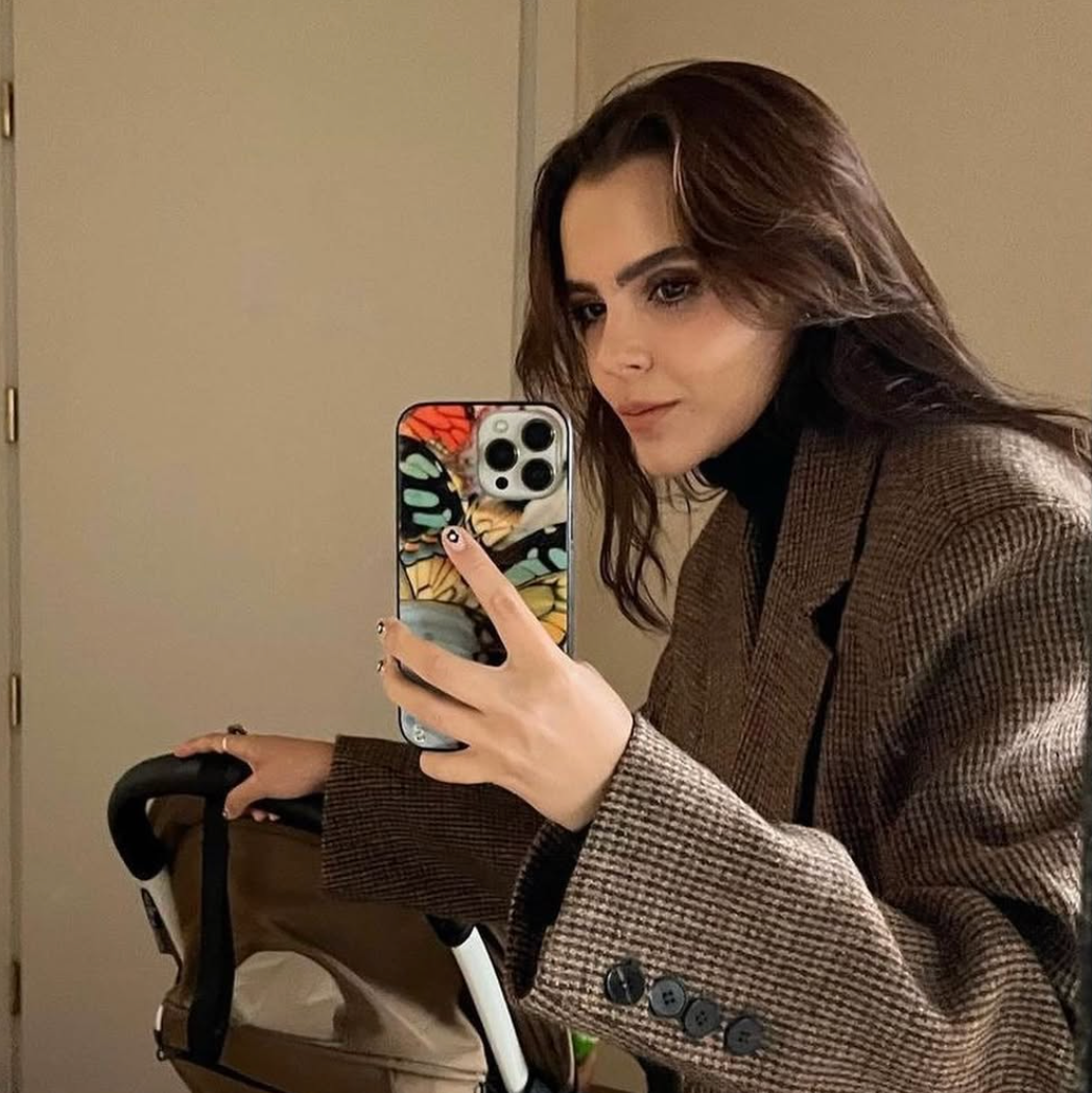 Woman taking a mirror selfie wearing a brown coat with a floral phone case.
